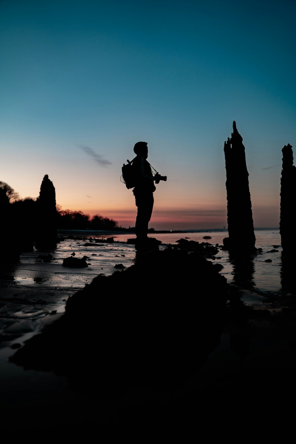 silhouette of man standing on rock near body of water during sunset