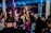 A crowded nightclub scene with people socializing and celebrating. Several individuals are holding bottles with sparklers attached, adding a festive and lively atmosphere. The club has dim lighting with colorful lights enhancing the party ambiance.