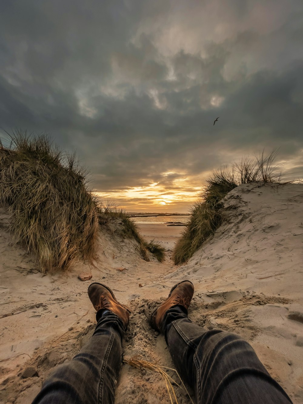 person in brown leather boots sitting on brown sand during daytime