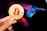 A hand holding a large gold coin with a prominent red Bitcoin symbol. The person's fingernails are painted orange, featuring small Bitcoin icons. In the background, there is a colorful, abstract design resembling a bull, using shades of purple, blue, pink, and black.