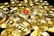 A collection of shiny gold coins featuring the Bitcoin symbol, with one prominent coin having a red Bitcoin symbol. The coins are stacked and scattered, reflecting light with a metallic sheen.