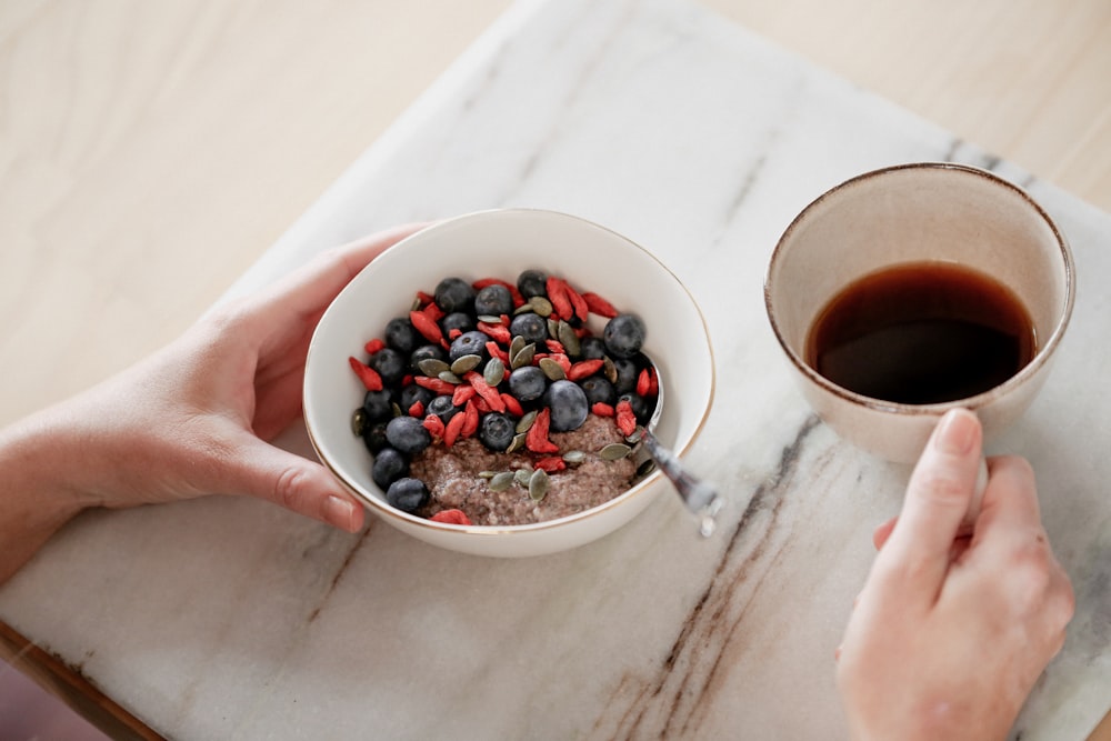 person holding white ceramic bowl with red and black berries