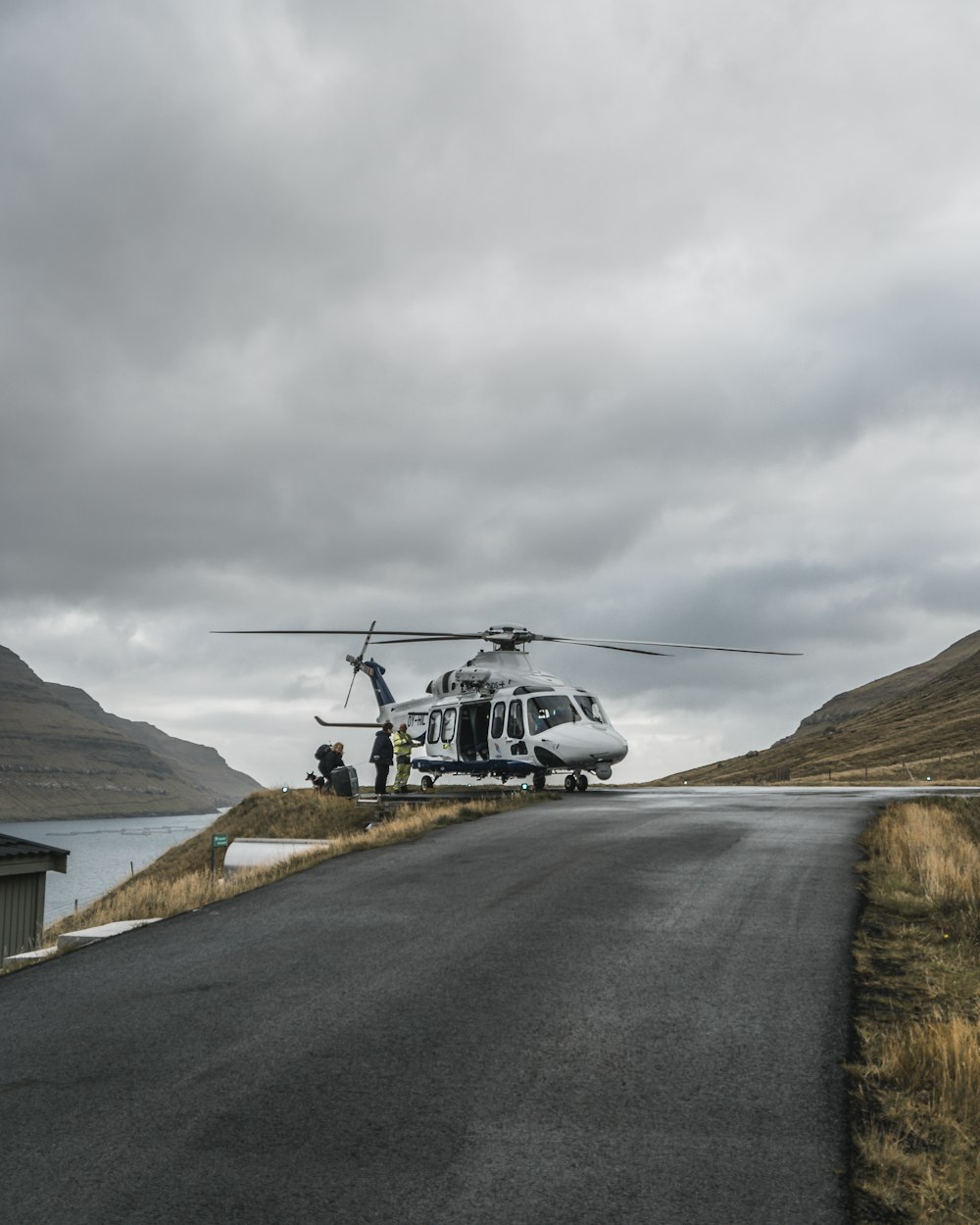 日中、灰色の空の下、ブラウンマウンテン近くの灰色のアスファルト道路を走る黒いヘリコプター