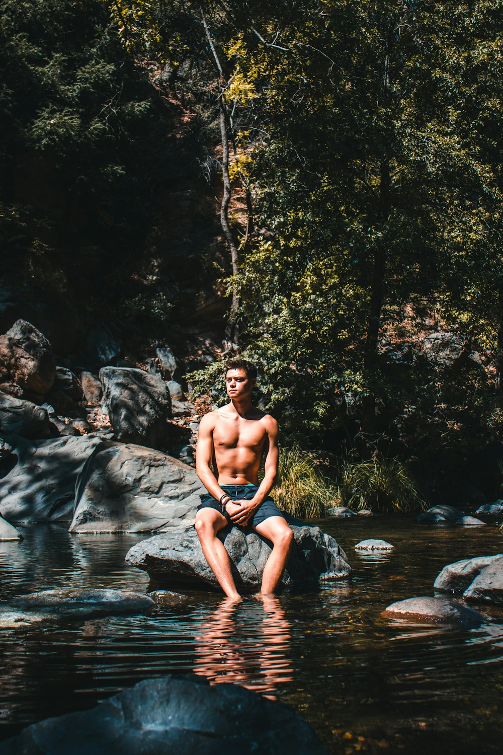 topless man sitting on rock in river during daytime