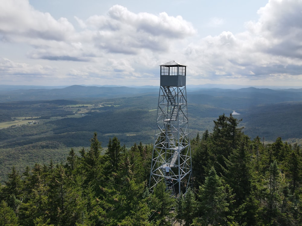 gray metal tower on green forest under white clouds during daytime