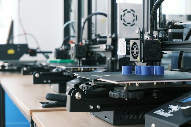 3D printer mid-print, extruding layers of white plastic filament to build a small object