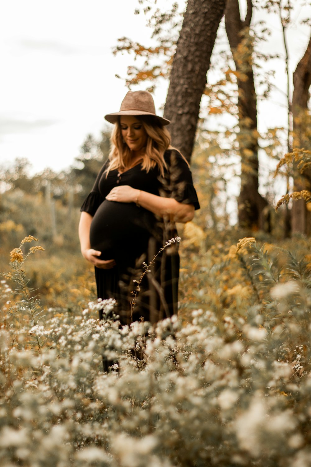 woman in black long sleeve shirt and brown hat standing on white flower field during daytime