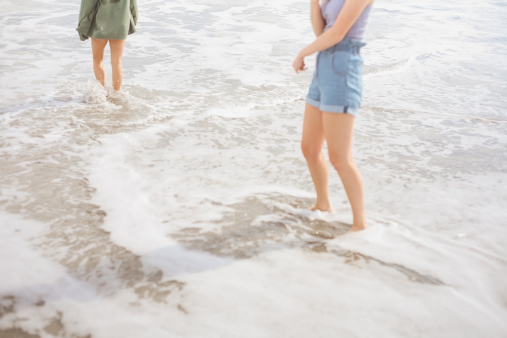woman in blue tank top and blue denim shorts walking on beach during daytime