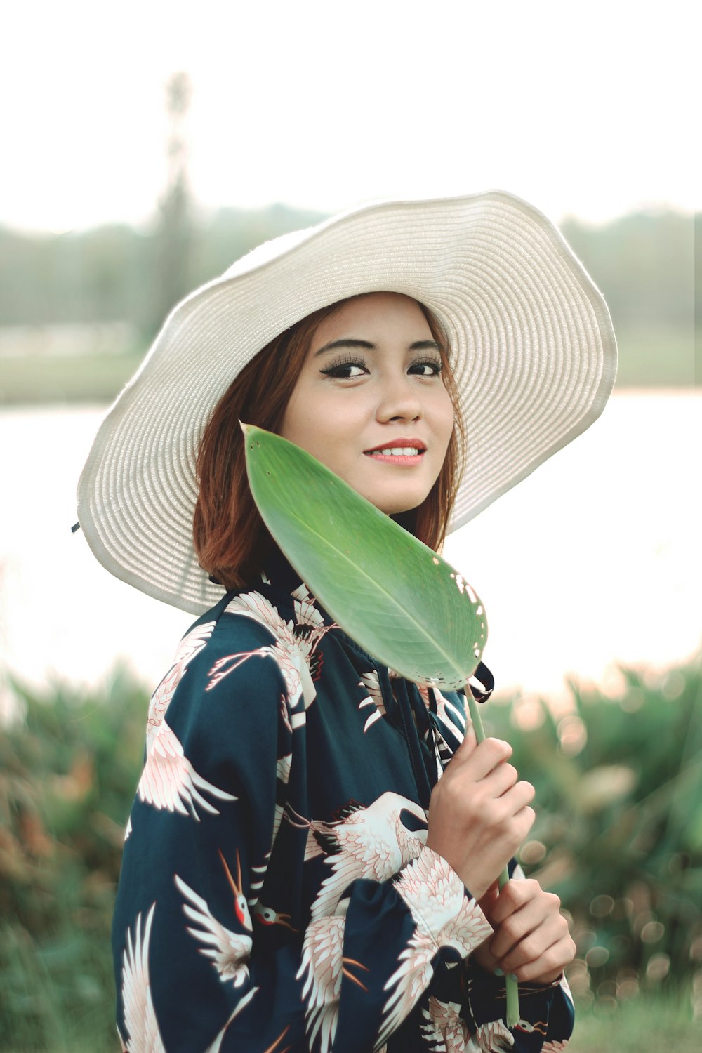 woman in white sun hat holding green leaf