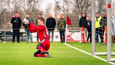 man in red and white jersey shirt playing soccer during daytime