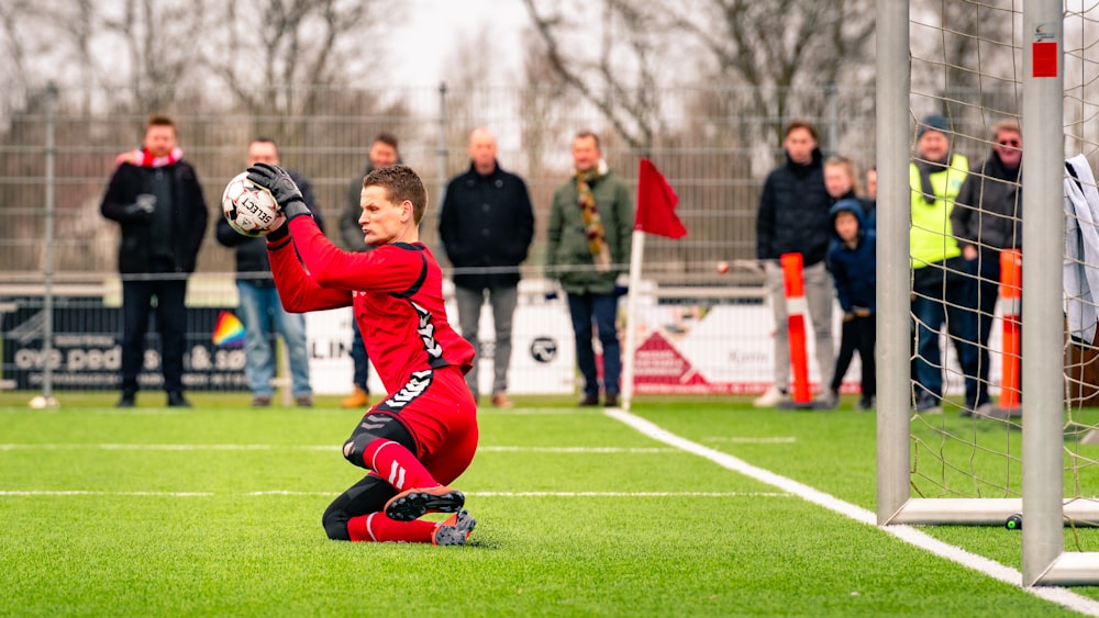 man in red and white jersey shirt playing soccer during daytime