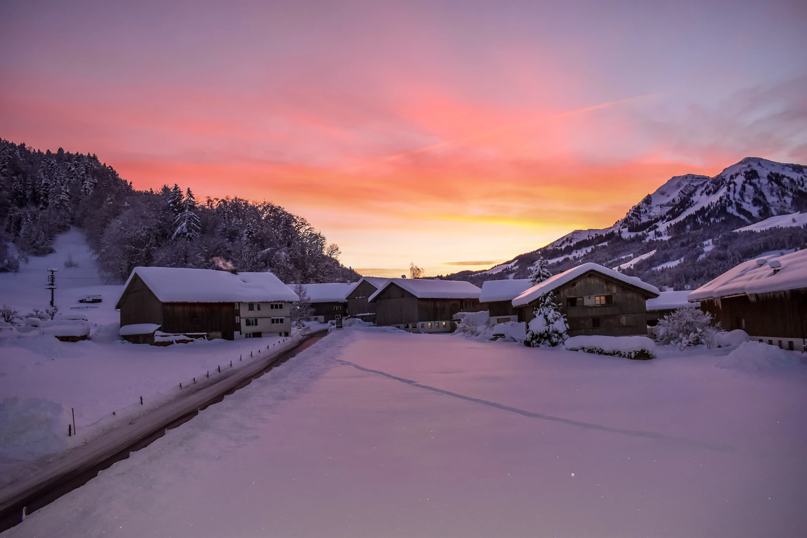 A pretty snow covered alpine village street with lit shops at dusk