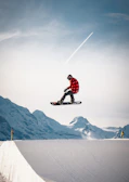 A snowboarder with a Triple Canber strapped on, holding three cans while catching air off a snowy jump