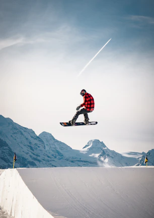 A snowboarder with a Triple Canber strapped on, holding three cans while catching air off a snowy jump