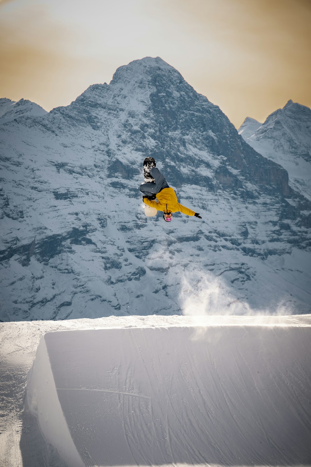 man in yellow jacket and black pants sitting on snow covered ground during daytime