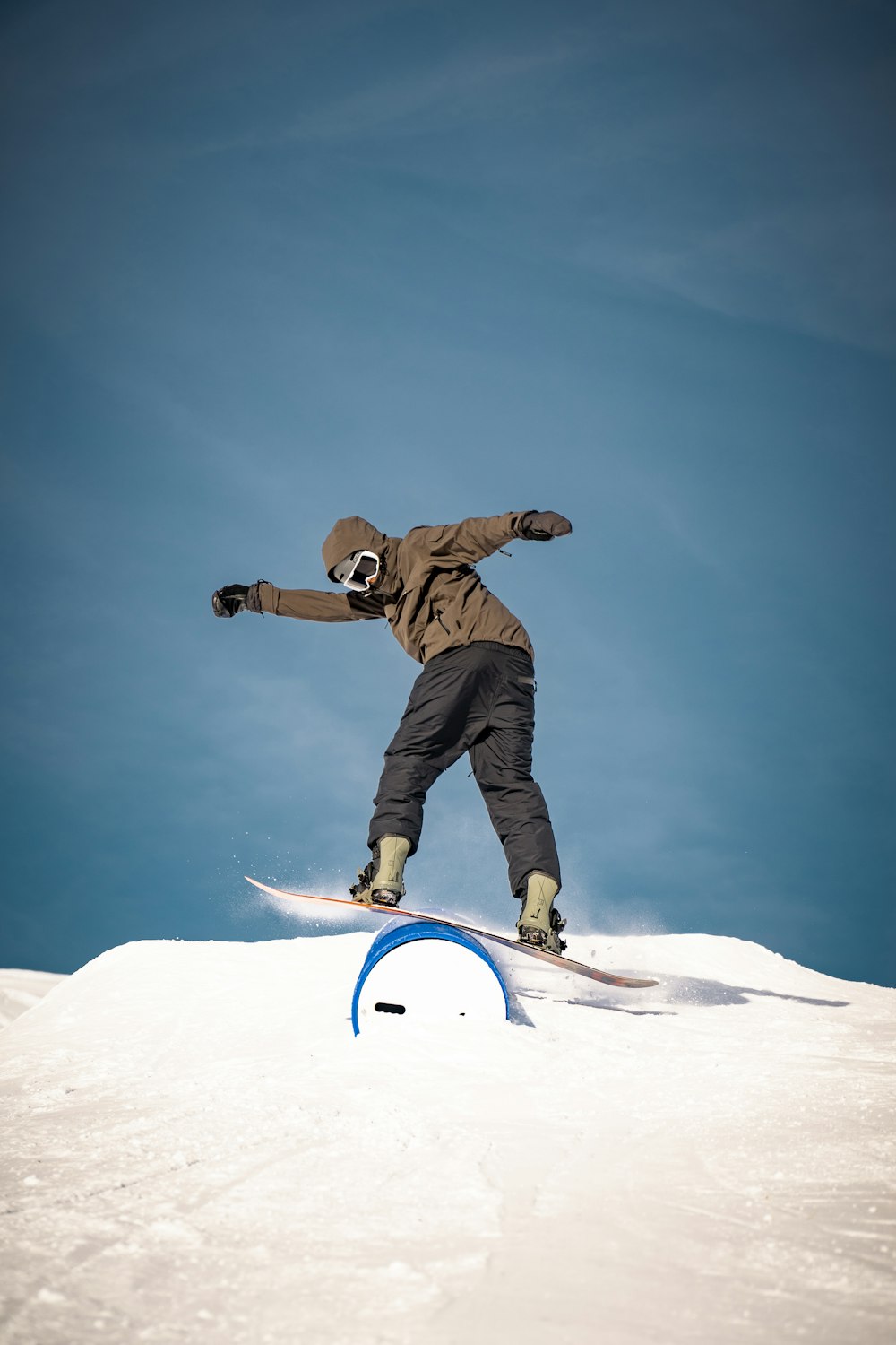 homme en veste marron et pantalon noir sur un snowboard blanc pendant la journée