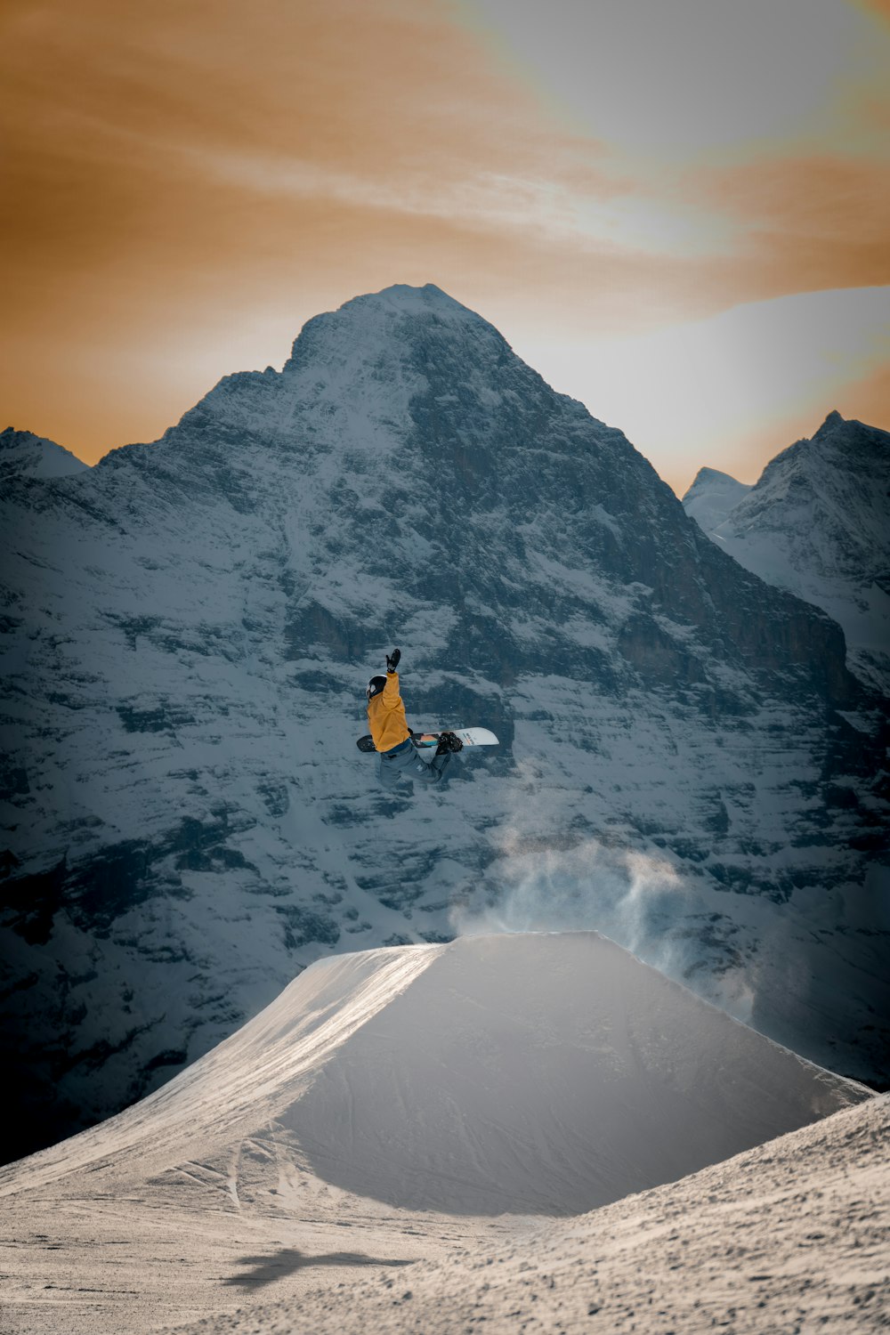 Persona en chaqueta amarilla sentada en la montaña cubierta de nieve durante el día