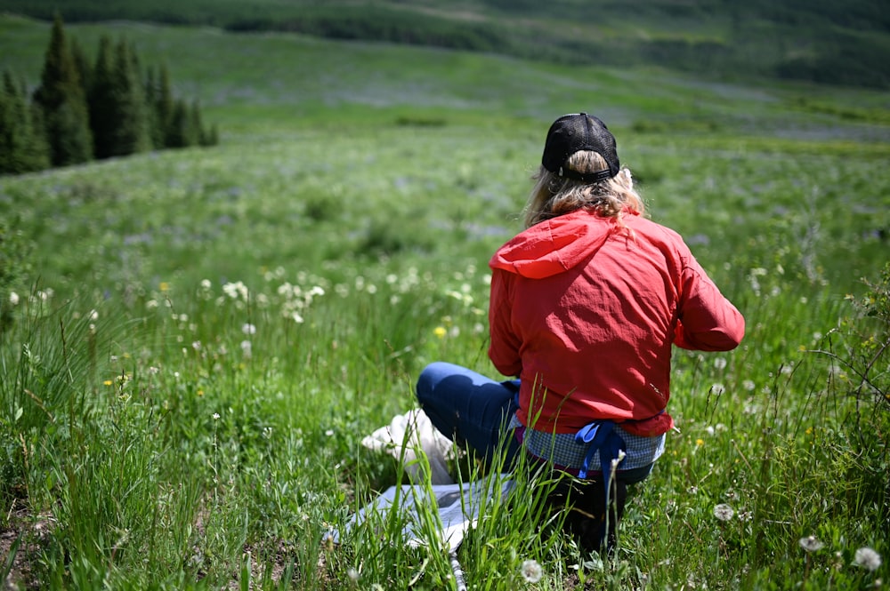 woman in red long sleeve shirt and blue denim jeans sitting on green grass field during