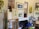 An artist's workspace with an easel holding a painting of a bird perched on a faucet. Multiple paintings hang on a wall, featuring nature scenes and abstract designs. The room is filled with art supplies, including brushes, canvases, and tools scattered around the area.