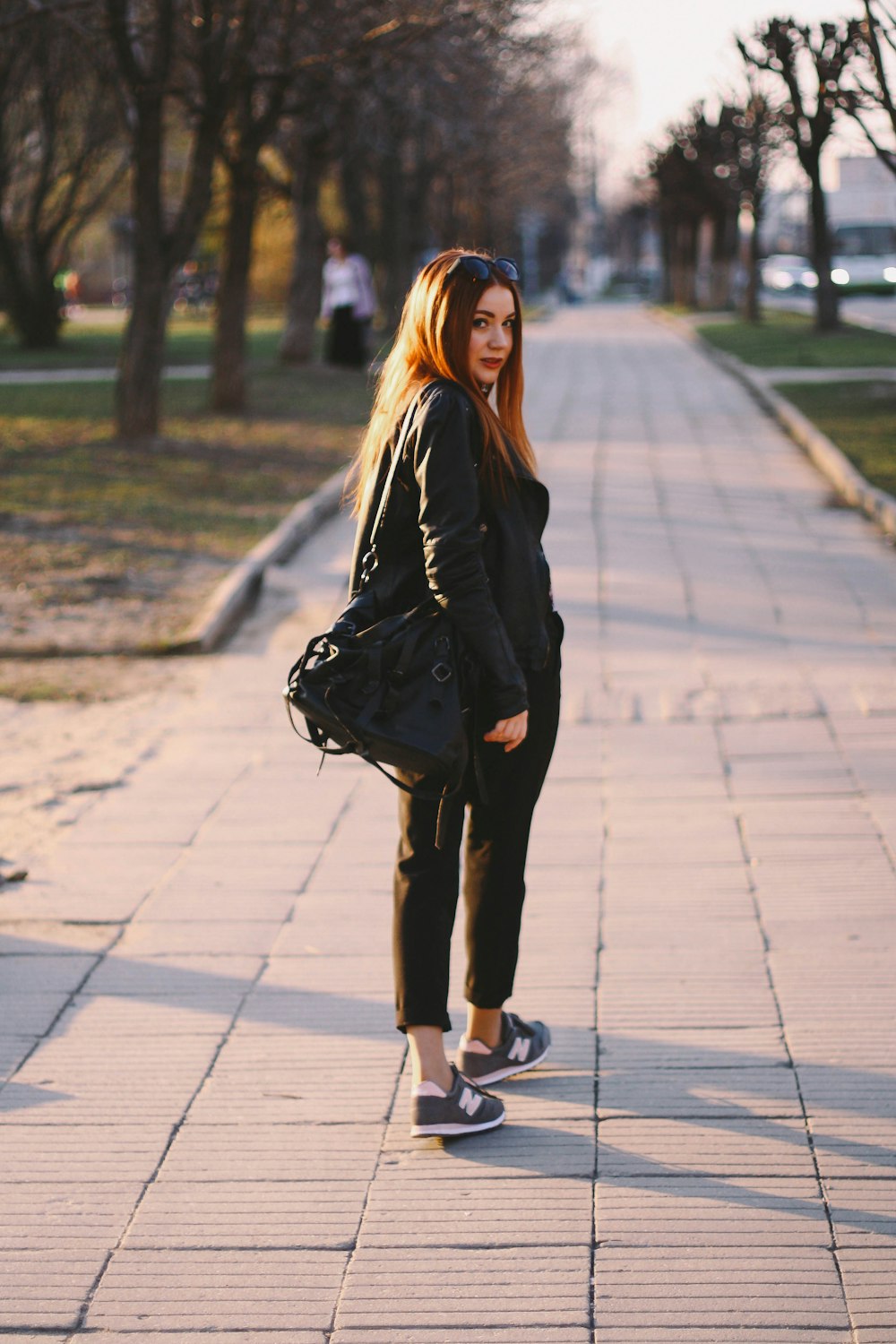 woman in black jacket and black pants standing on sidewalk during daytime
