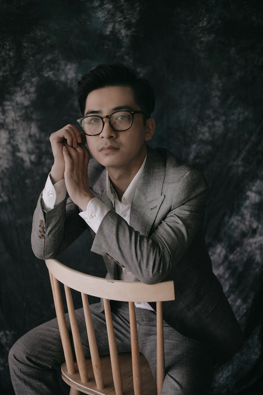 woman in black framed eyeglasses and green blazer sitting on brown wooden chair