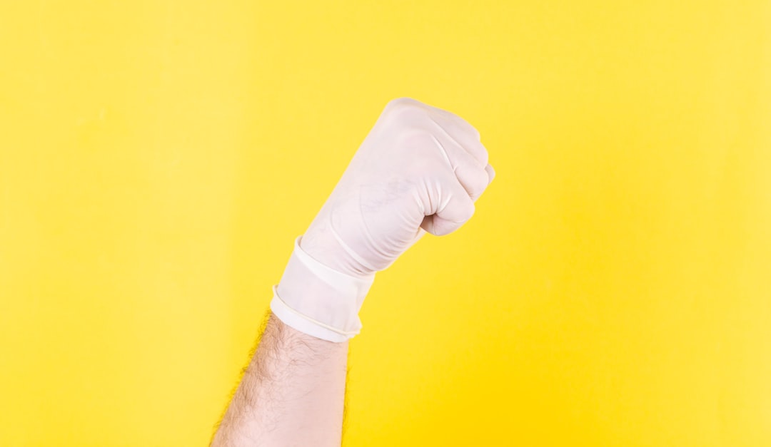person in white long sleeve shirt holding hand of person in white long sleeve shirt, Fist of a doctor in a white medical glove on a yellow background. The medicine. Successful operation. The doctor is a hero. Covid 19. Place for an inscription. Advertising. Coronavirus.