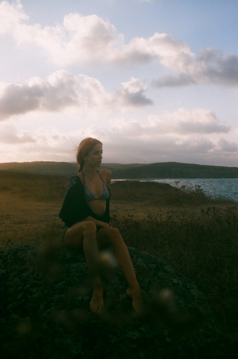 woman in black bikini sitting on rock near body of water during daytime