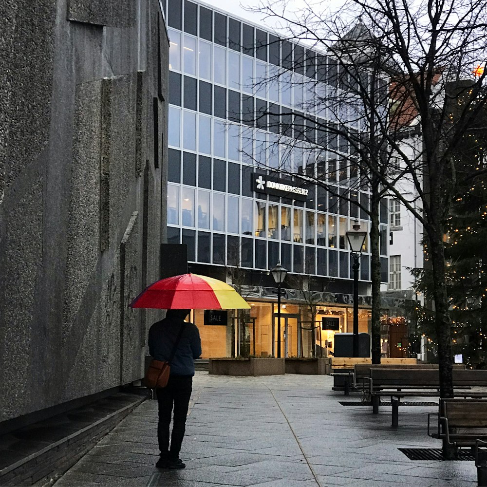 person in black jacket and black pants holding umbrella walking on sidewalk during daytime