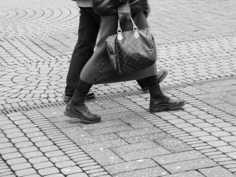 Frau in schwarzem Mantel und schwarzer Ledertasche tagsüber auf dem Bürgersteig spazieren