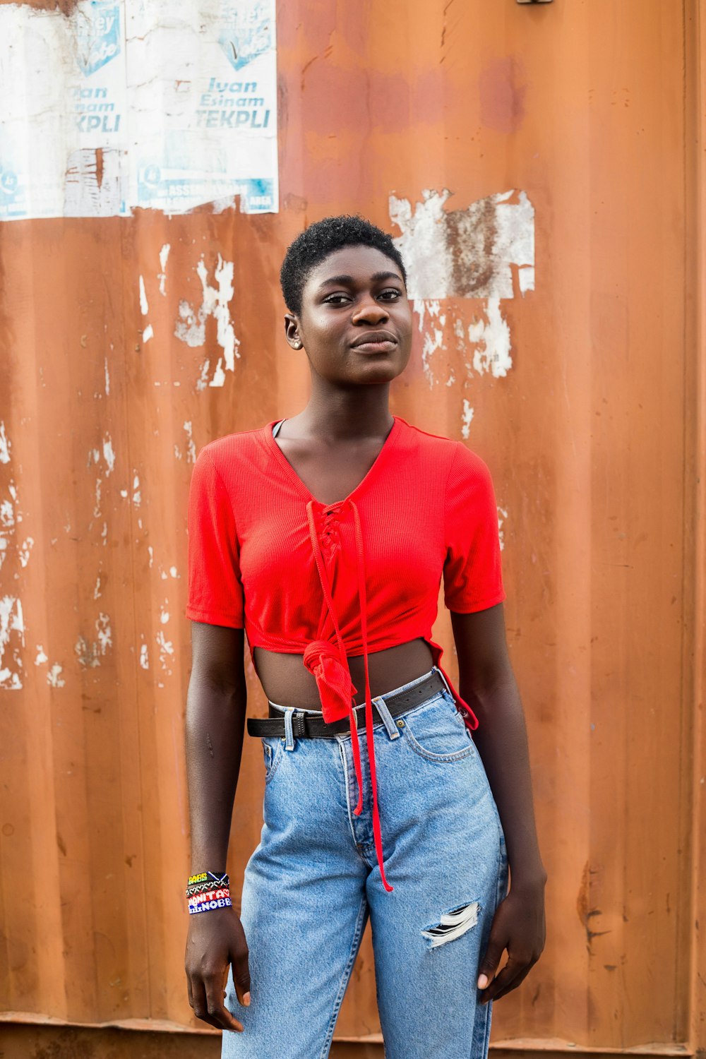 Woman in red crew neck t-shirt and blue denim jeans standing beside brown wooden door photo – Free #youth #fashion #fashiongirl #fashion Image on Unsplash