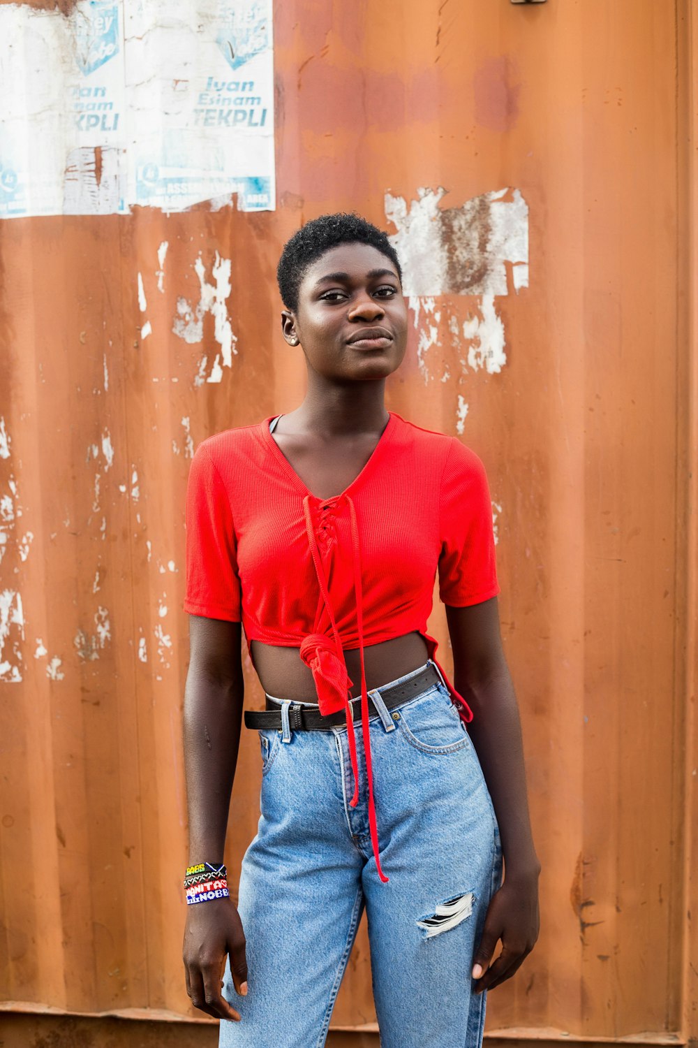 woman in red crew neck t-shirt and blue denim jeans standing beside brown wooden door