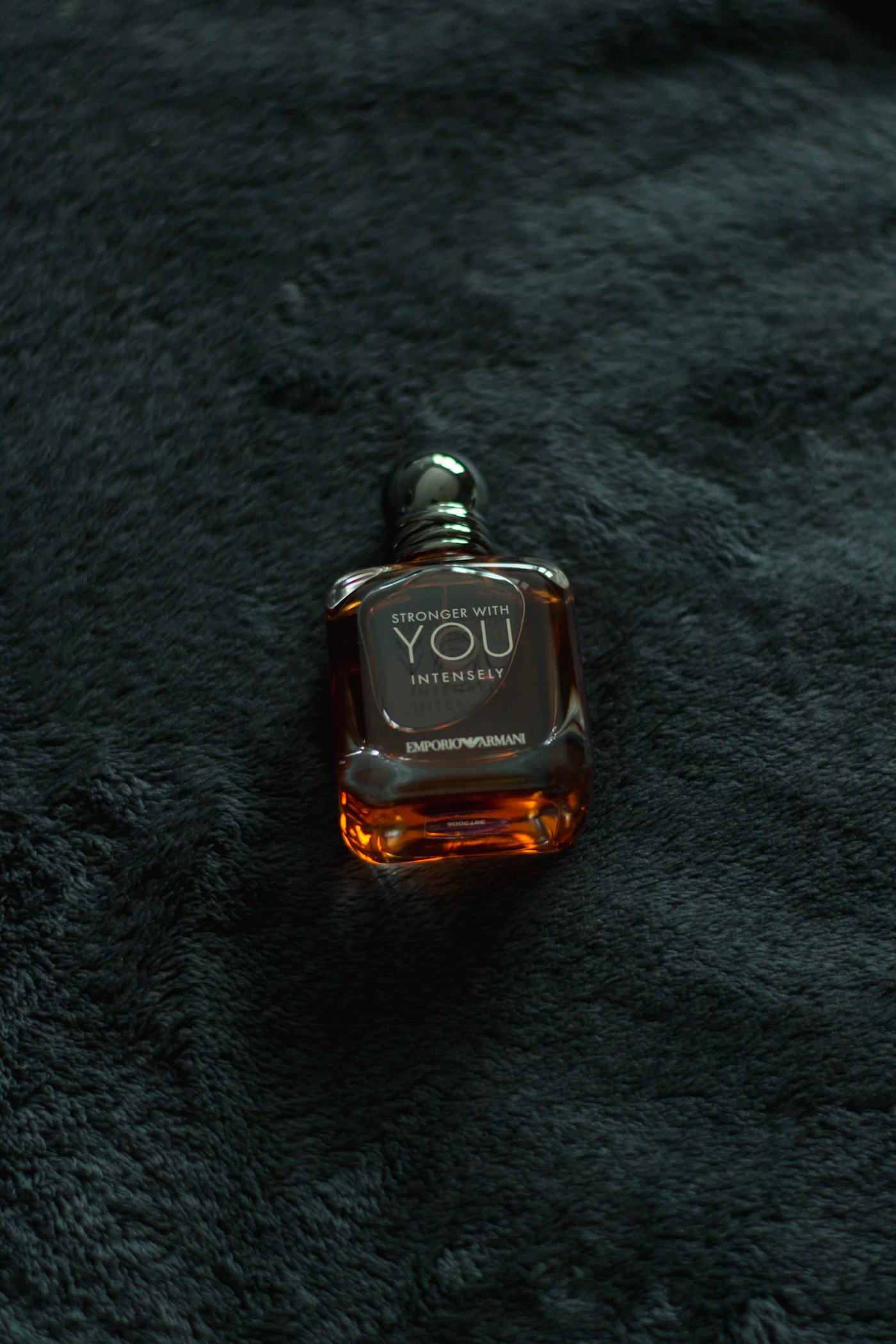 Perfume masculino oscuro sobre tejido negro en un ambiente invernal