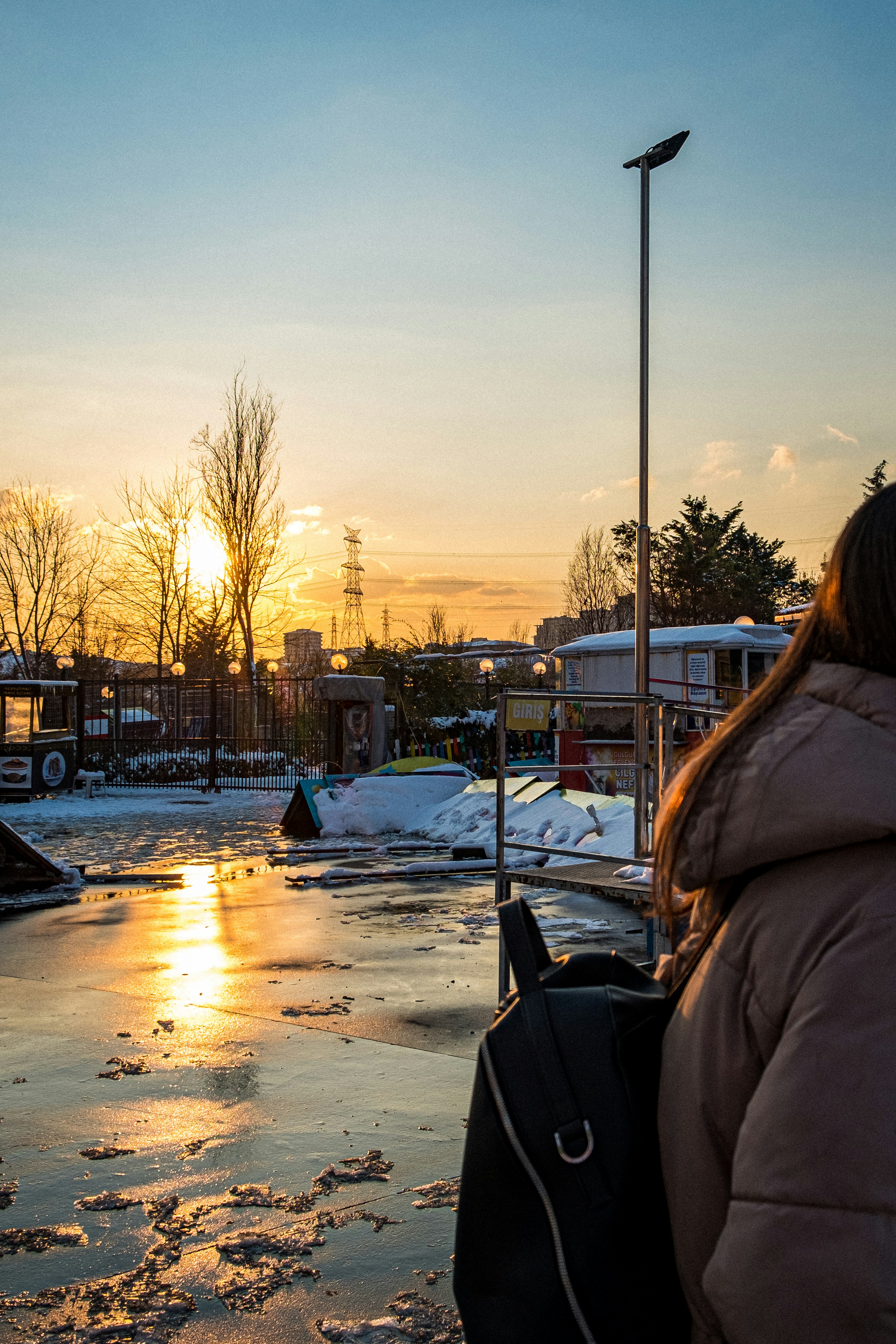 Mujer en chaqueta marrón de pie en el suelo cubierto de nieve durante la puesta del sol