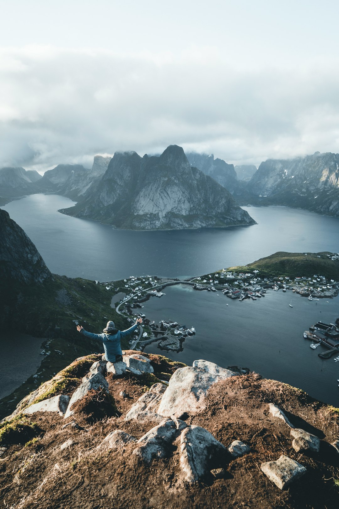 person in blue jacket and blue denim jeans sitting on rock near lake during daytime