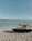 Jet skis are parked on a sandy beach with turquoise ocean water in the background. The sky is clear with a few scattered clouds.