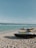 Jet skis are parked on a sandy beach with turquoise ocean water in the background. The sky is clear with a few scattered clouds.