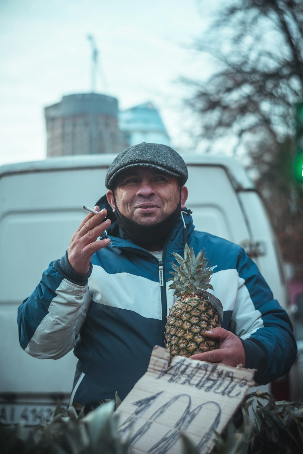 homme en veste bleue et bonnet en tricot gris tenant un fruit d’ananas