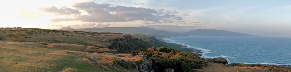 grüner und brauner Berg neben blauem Meer unter weißen Wolken tagsüber