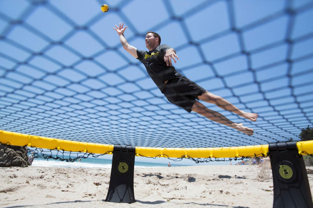 girl in black shirt and black pants jumping on yellow and blue net