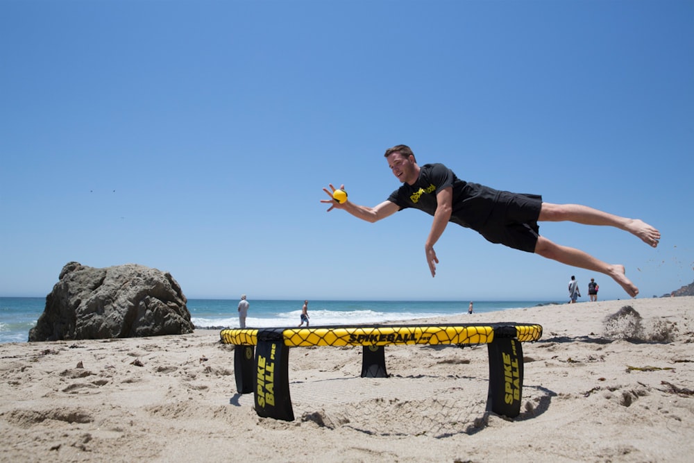 man in black t-shirt and blue denim jeans jumping on beach shore during daytime