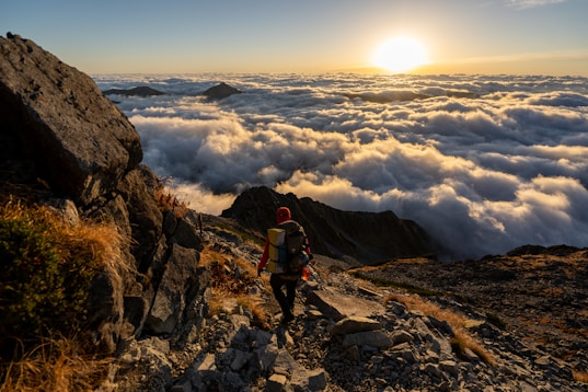 man in red jacket and black pants standing on rocky mountain during daytime