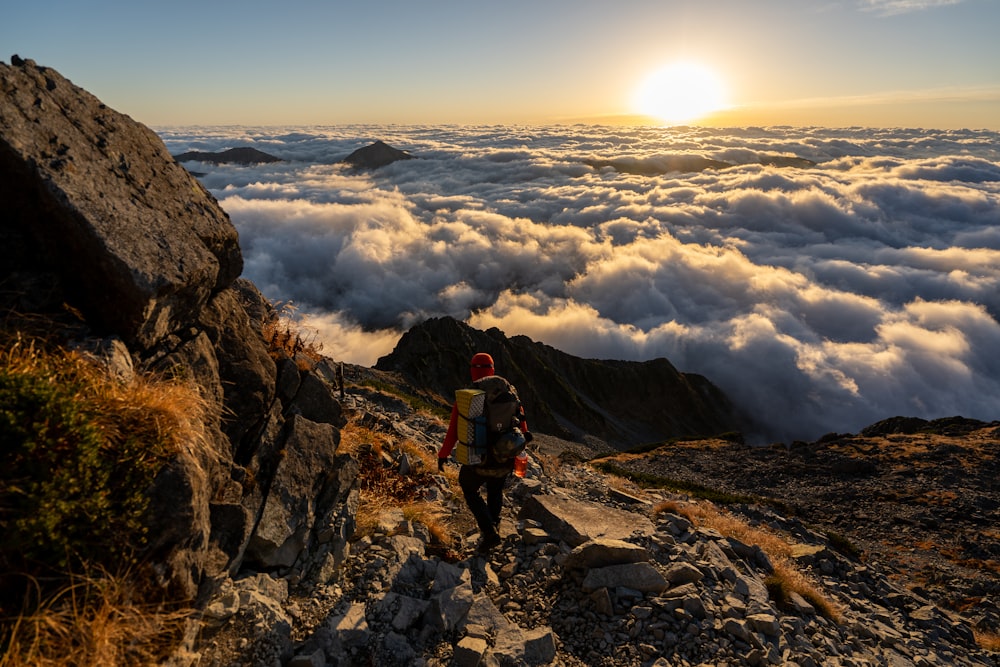 man in red jacket and black pants standing on rocky mountain during daytime