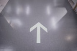 A glossy floor with a white arrow pointing upward, reflecting lights from the ceiling.