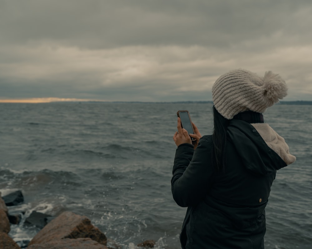 man in black jacket taking photo of sea during daytime
