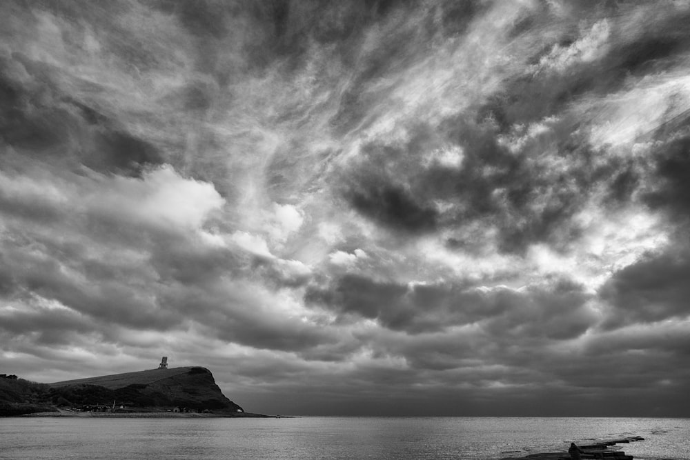 grayscale photo of body of water under cloudy sky