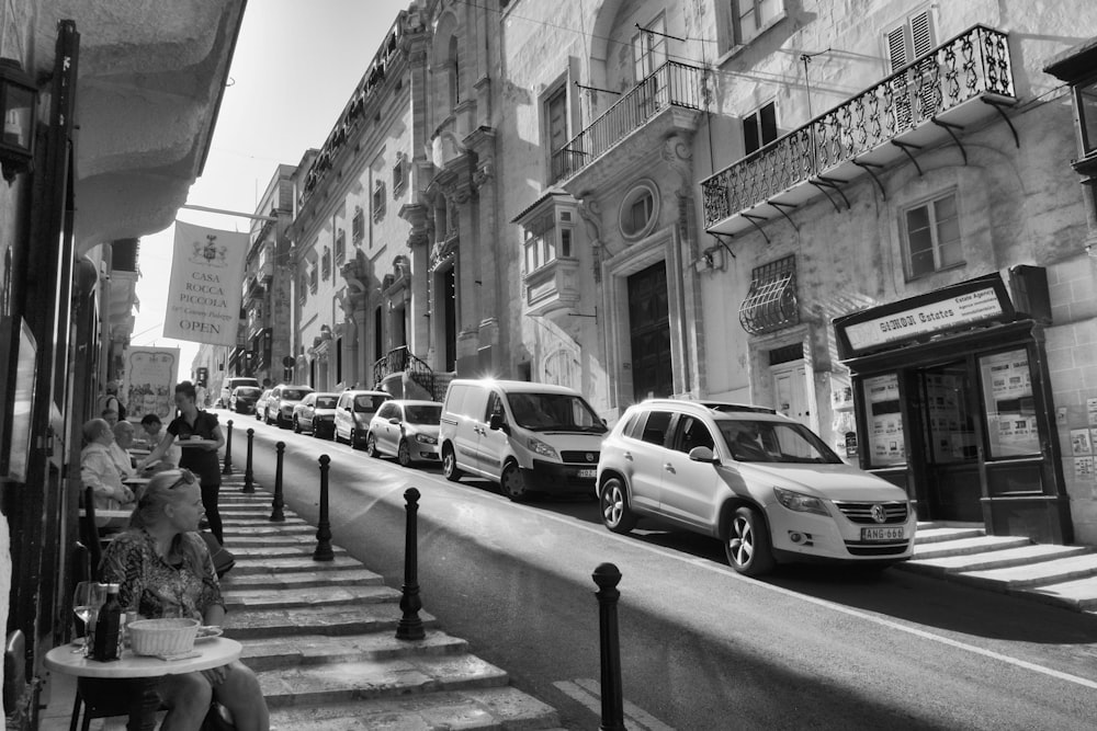 grayscale photo of cars parked on sidewalk