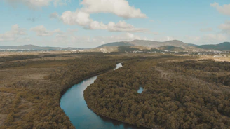 A winding river cutting through dense jungle with mountains in the background.