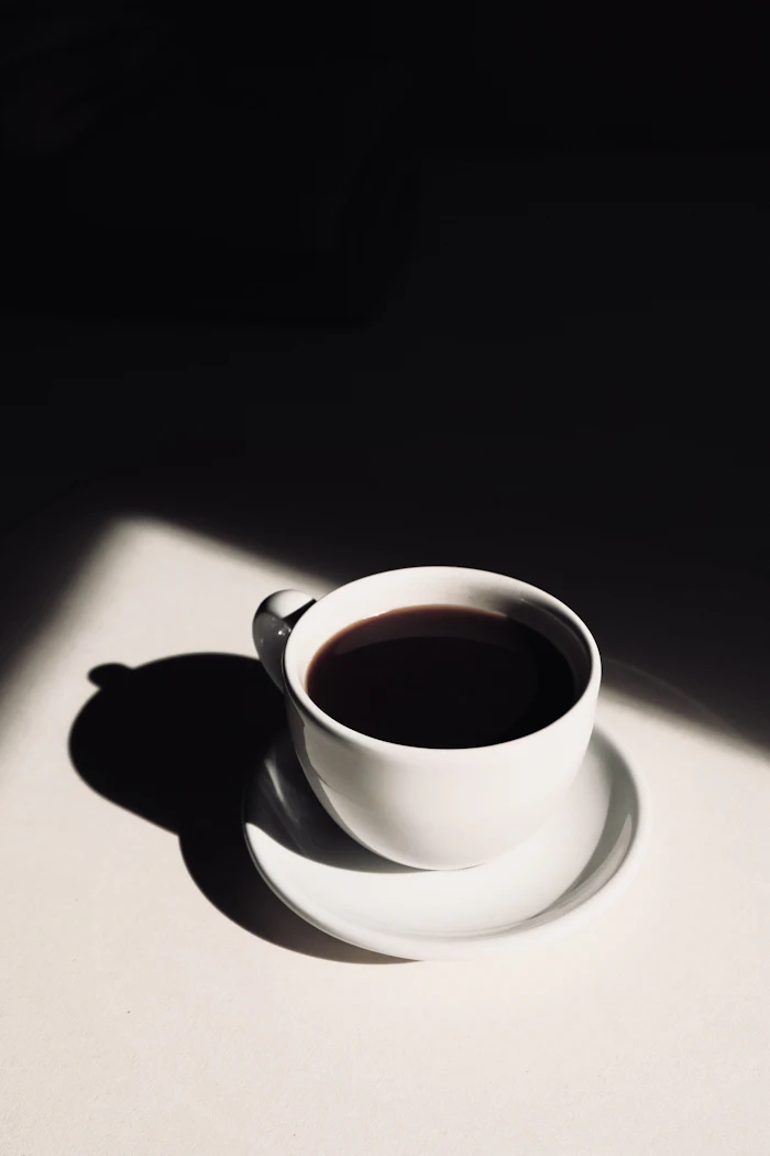 A white cup of black coffee casting a long hard shadow