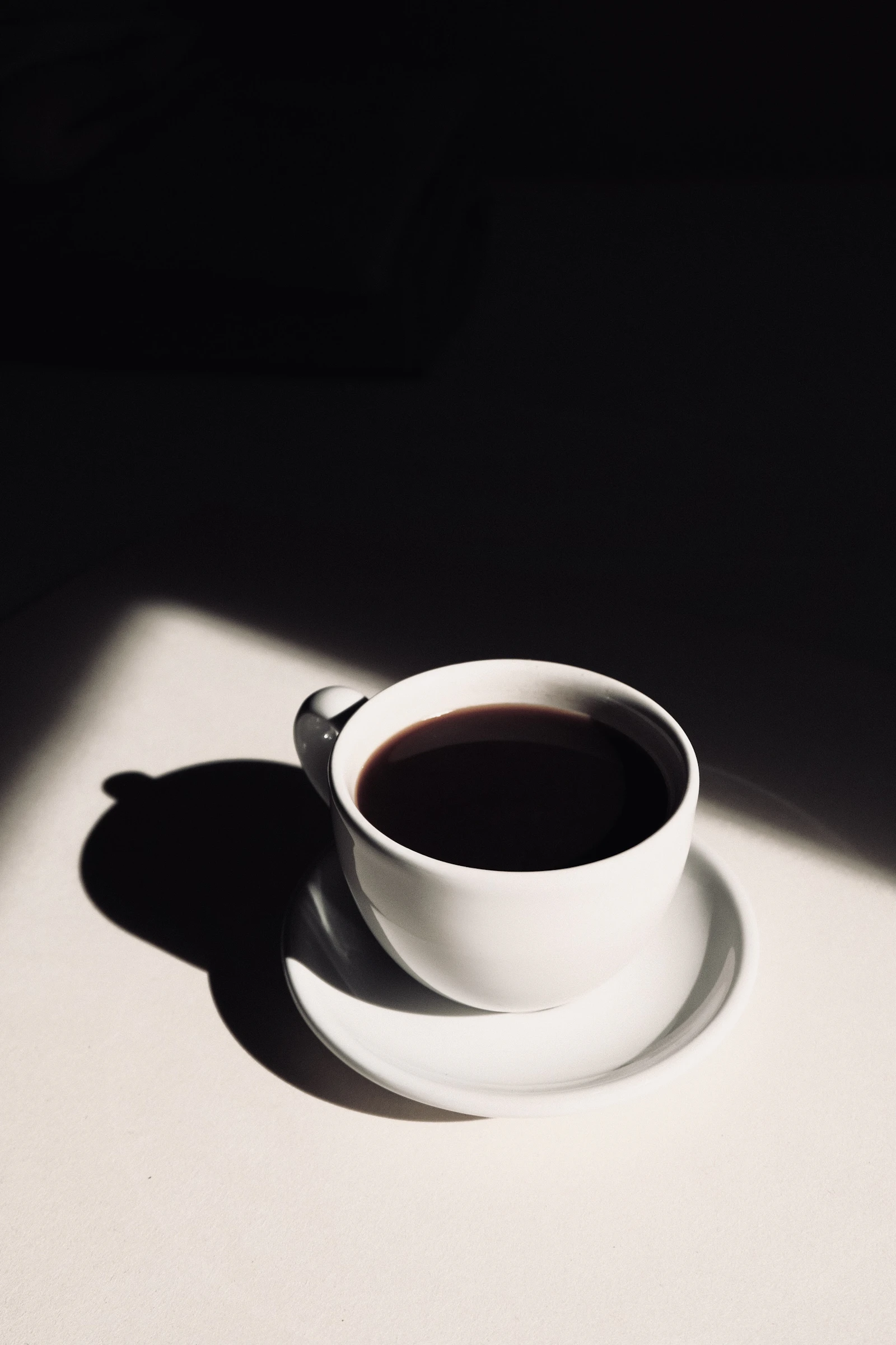 Tasse de café noir sur une soucoupe blanche, lumière du matin