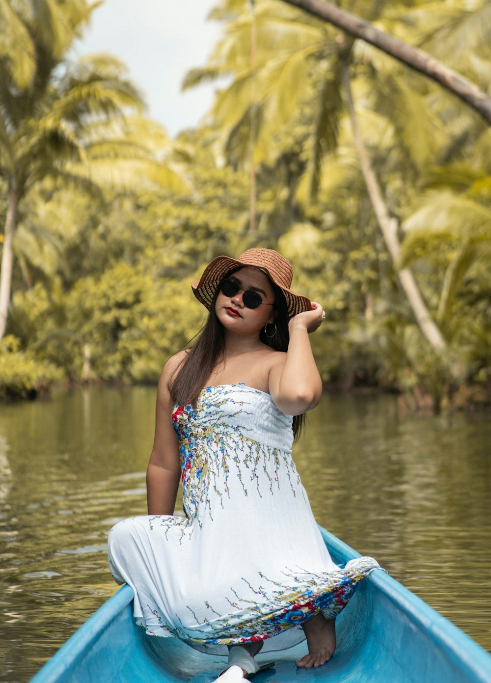woman in white dress wearing black sunglasses sitting on blue hammock near body of water during